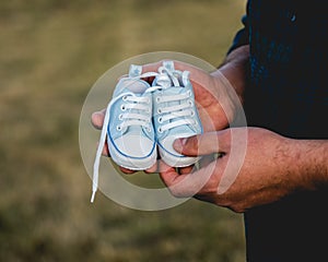 Man`s hands holding a pair of blue and white baby shoes