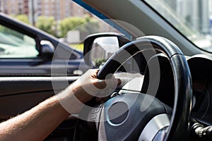 Man`s hands holding steering wheel while driving car on city road