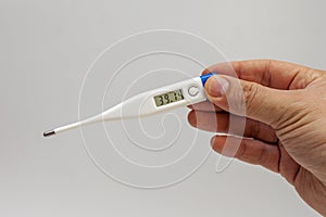 Man`s hands holding white electronic thermometer indicating high temperature. Virus alert