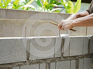 Man`s hands  of industrial bricklayer with  steel bar installing brick blocks on construction site