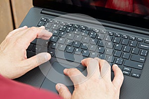 The man's hands on the keyboard of the laptop computer stacked in his lap.