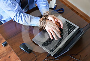 Man`s hands in old rusty chains. In the trap of office work. Routine job. Manager near the laptop