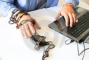 Man`s hands in old rusty chains. In the trap of office work. Routine job. Manager near the laptop