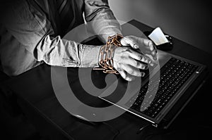 Man`s hands in old rusty chains. In the trap of office work. Routine job. Manager near the laptop