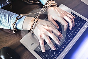 Man`s hands in old rusty chains. In the trap of office work. Routine job. Manager near the laptop