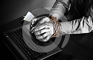 Man`s hands in old rusty chains. In the trap of office work. Routine job. Manager near the laptop