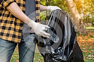 Man`s hands pick up plastic bottles, put garbage in black garbage bags to clean up at parks, avoid pollution, be friendly to the