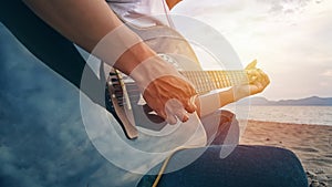 Man`s hands playing acoustic guitar, capture chords by finger on sandy beach at sunset time. playing music concept