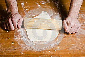 Man's hands rolled dough with wooden rolling pin on the wooden table.