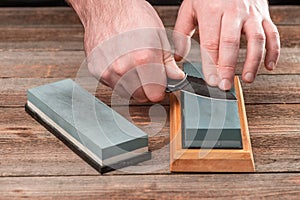 Man`s hands sharpening a pocket knife with a whetstone on a wooden table