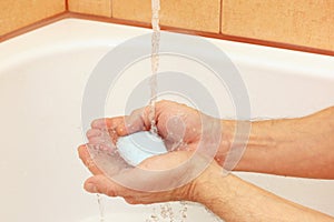 Man`s hands with soap under running water in bathroom