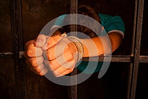 Man's hands tied with rope behind the bars