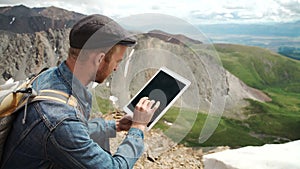 Man's hands touching screen of digital tablet on the background of mountains