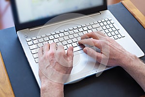 Man`s hands typing on laptop keyboard at the desk