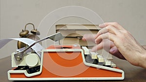 Man`s hands typing on a red retro typewriter on a table with books