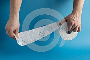 Man`s hands unwind a piece of toilet paper from a roll on a blue background. Place for text. hygiene