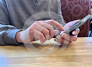 A Man's Hands Use a Smart Phone at a Table