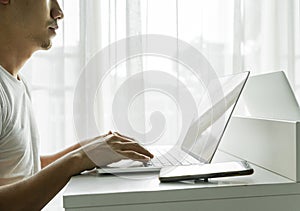 Man's hands using laptop computer with smartphone on white table at home. Online shopping, home work, freelance