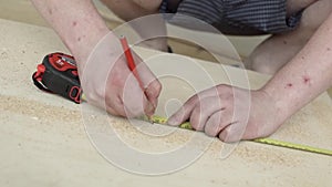 Man`s hands with yellow ruler and red pencil making marks on wooden plank