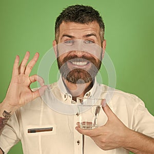 Man`s health. Man with long beard hold water glass on green background.