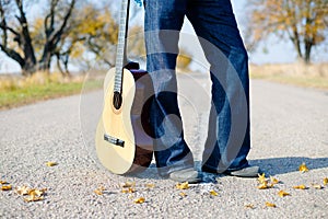Man's legs in jeans with guitar empty country road