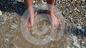 Man`s legs on rocky beach. Concept. Close-up of man standing on Bank and wetting feet. Feet stand on shore pebbles with