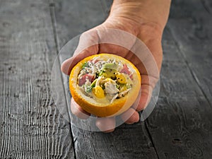 The man`s right hand holds half an orange filled with salad.