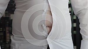 A man's shirt buttons are unbuttoned on his stomach due to a fat belly and obesity. Tight clothes, overweight. Slow