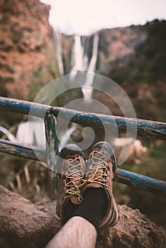 ManÂ´s trekking shoes in a nature of Morocco - Ouzod falls. Close up of hiking boots against waterfall.