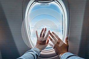 Man`s and woman`s hands inside touching window of airplane with clouds and blue sky background . Traveling and vacation concept.