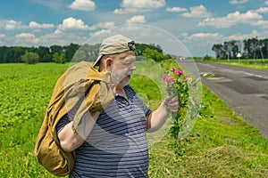 Man with sack and bunch of wild flowers standing on a roadside in central Ukraine