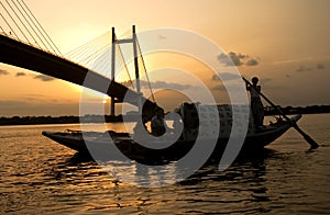 Man sailing boat at sunset near a bridge