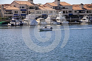 A man sailing a small motor boat at Huntington Harbour with boats and yachts docked in Huntington Harbour and homes