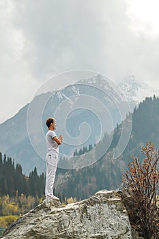 A man in a Samasthiti pose on a stone among a mountain lake