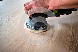 Man sanding wood with orbital sander in a workshop