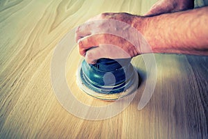 Man sanding wood with orbital sander in a workshop