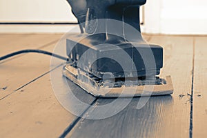 Man sanding wooden floor with an electric sander.