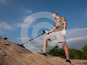 Man on a sandy ground with a metal detector looking for treasure on a sunny summer day