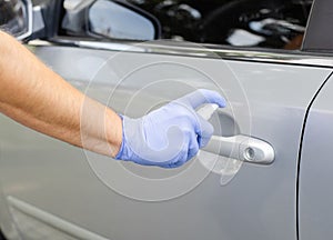 Man sanitizing door handle of his car outdoors.  Male hand in protective glove holding sanitizer closeup