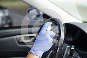 Man sanitizing wheel and salon of his car.  Male hand in protective glove holding sanitizer closeup