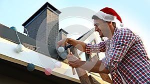 Man in Santa hat decorating house with Christmas lights