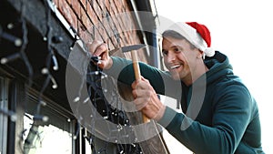 Man in Santa hat decorating house with Christmas lights