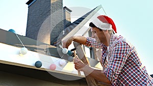 Man in Santa hat decorating house with Christmas outdoors