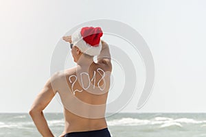 Man in Santa hat with the inscription 2018 on the back standing on the beach and looks into the distance