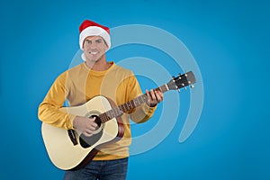 Man in Santa hat playing acoustic guitar on light blue background. Christmas music