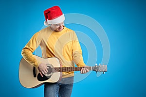 Man in Santa hat playing acoustic guitar on light blue background, space for text. Christmas music