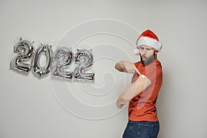 A man in a Santa hat is showing plaster after vaccination near balloons