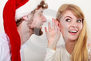 Man in santa hat whispering to woman ear