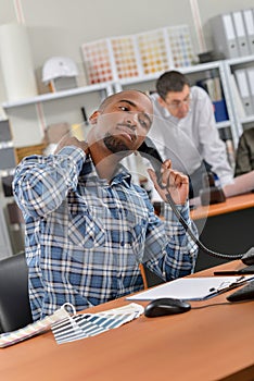 Man sat at desk on telephone stretching neck