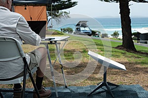 man with satellite internet dish connected working on computer at remote beach side campsite